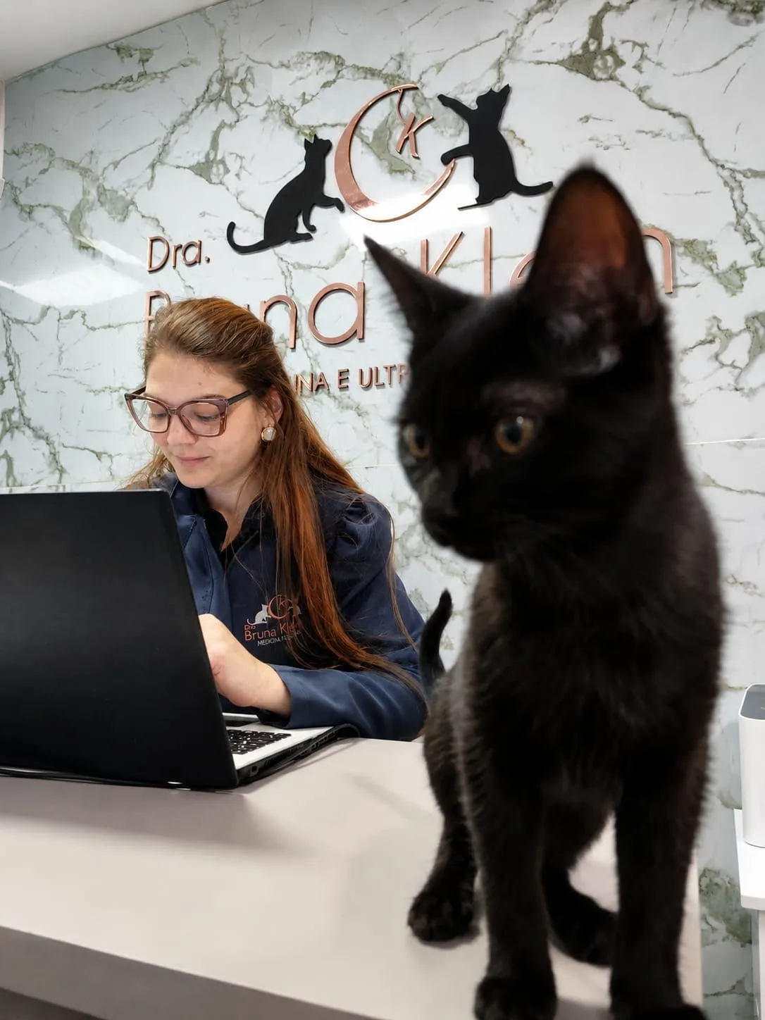 Dra. Bruna Klein na recepção da clínica com um gato preto em primeiro plano